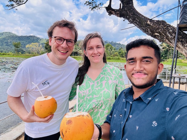 Travellers holding king coconuts beside a lake